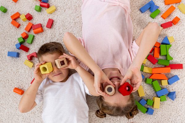 Two children lying on a rug playing with coloured wooden blocks